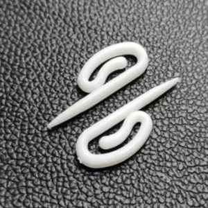 Two white curtain hooks displayed on a textured black background, showcasing their durable and modern design.